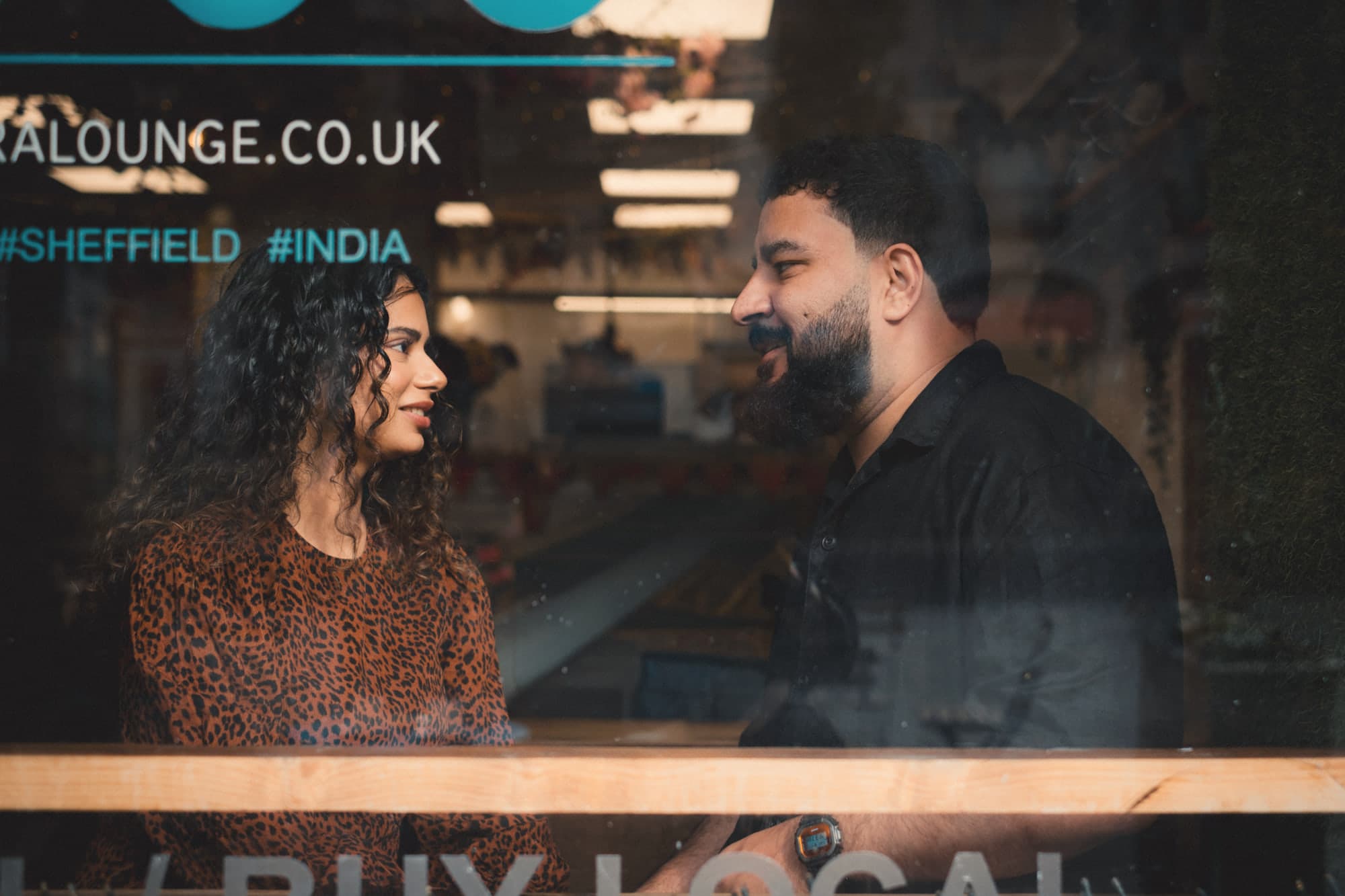 The two of them talking, seen through a café window lettered #SHEFFIELD #INDIA